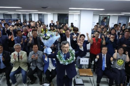 图为16日晚,首尔市教育监补选中进步阵营唯一一位候选人郑根埴在首尔麻浦区的竞选活动中确定当选后,戴着花环欢呼。【照片来源:NEWS1】